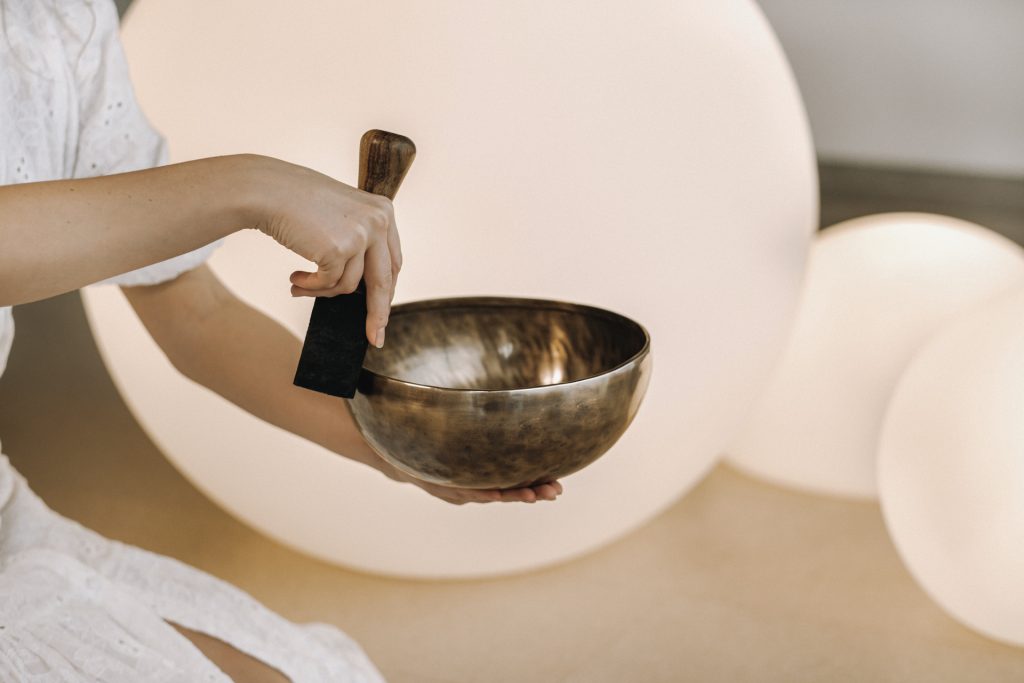 Person hält eine Klangschale und Klöppel vor hellen, runden Lichtern.