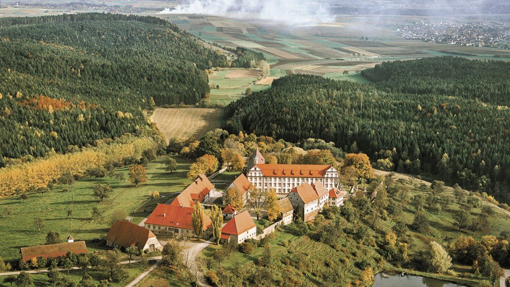 Luftaufnahme eines Klosters inmitten von Wäldern und Feldern im Schwarzwald, umgeben von herbstlicher Landschaft.