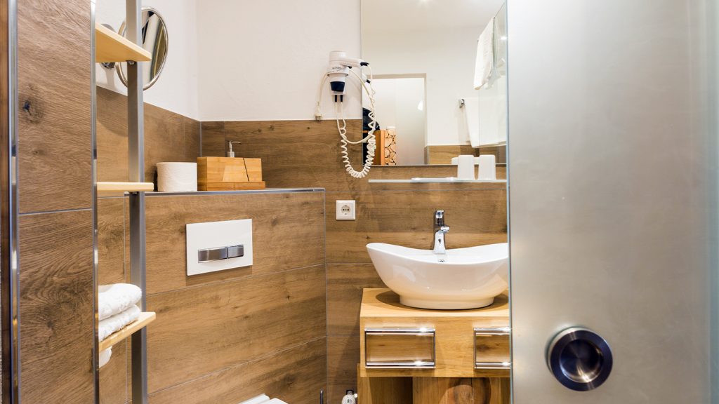 Modernes Badezimmer mit Holzverkleidung, Waschbecken, Spiegel und Haartrockner.