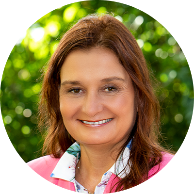 Porträt einer lächelnden Frau vor verschwommenem grünen Hintergrund, in rosa Jacke.